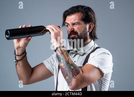 Auf der Suche nach dem letzten Tropfen. Brutaler Barkeeper in Fliege. Eleganter Barkeeper. Hübscher Hipster trinkt Weinglas. Sommelier schmeckt Alkohol. Bärtiger Mann in Hosenträgern trinkt Rotwein. Stockfoto