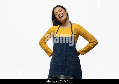 Junge Frau lächelt, während sie eine Schürze mit Wok trägt Vorne Stockfoto