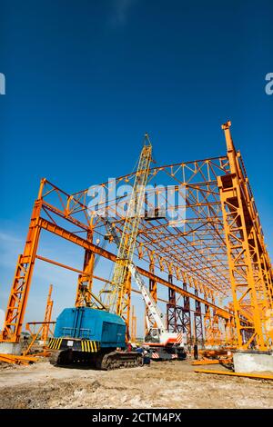 Kostanay/Kasachstan - Mai 14 2012: Bau eines neuen Fabrikgebäudes mit orangefarbener Stahlkonstruktion. Gelber Trägerkran und Arbeiter im Bau suspen Stockfoto