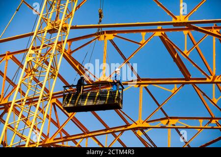 Kostanay/Kasachstan - Mai 14 2012: Bau eines neuen Fabrikgebäudes mit orangefarbener Stahlkonstruktion. Zwei Höhenarbeiter im Bau suspendierten cr Stockfoto