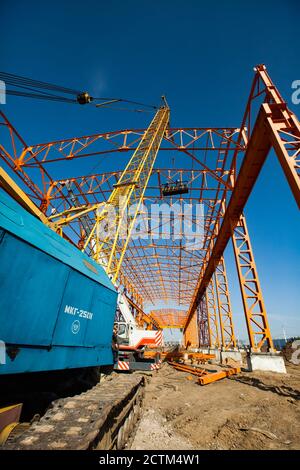 Kostanay/Kasachstan - Mai 14 2012: Bau eines neuen Fabrikgebäudes aus orangefarbenem Stahl. Gelber Trägerkran und Arbeiter in constructi Stockfoto