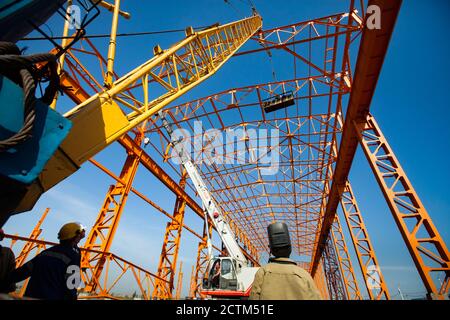 Kostanay/Kasachstan-Mai 14 2012: Bau eines neuen Fabrikgebäudes orange Stahlkonstruktion. Gelber Trägerkran und Arbeiter in Bauspanner Stockfoto