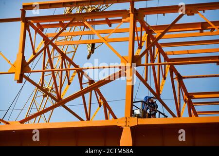 Kostanay/Kasachstan - Mai 14 2012: Bau eines neuen Fabrikgebäudes aus orangefarbenem Stahl. Zwei Arbeiter in der aufgehängten Wiege. Stockfoto