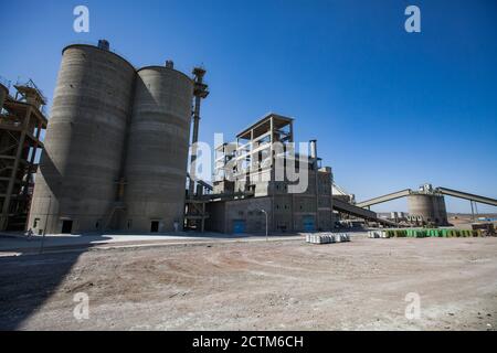 Mynaral/Kasachstan - April 23 2012: Moderne Zementanlage in der Wüste. Zementsilos oder Turm, Fabrikgebäude, Asphaltstraße und Förderband auf klaren blauen sk Stockfoto