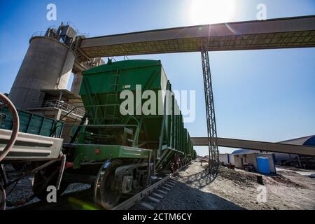 Mynaral/Kasachstan - April 23 2012: Zementanlage von Jambyl. Güterbahnterminal. Eisenbahnwaggons und Laderförderer auf blauem Himmel mit Sonne. Stockfoto