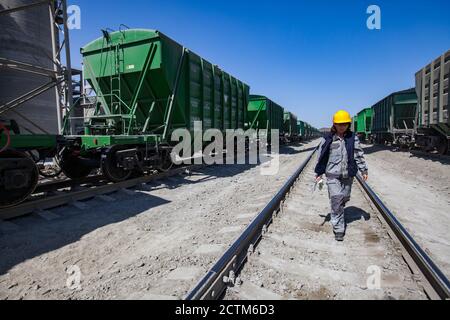 Mynaral/Kasachstan - April 23 2012: Zementanlage von Jambyl. Güterbahnterminal. Arbeiterinnen in gelber Mütze und Arbeitskleidung tragen auf den Schienen. Stockfoto