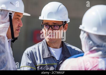 Mynaral/Kasachstan - April 23 2012: Zementanlage von Jambyl. Drei Spezialisten für weiße Helme und Schutzanzüge sprechen. Stockfoto