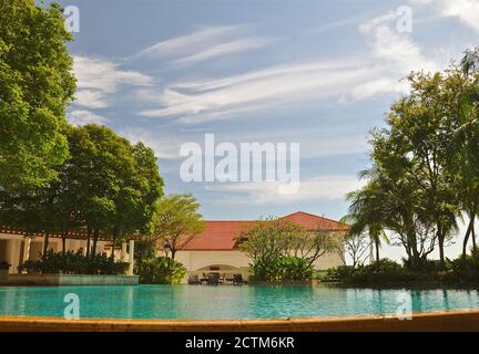 Luxuriöse Umgebung mit ruhigem blauem Wasser in einem tropischen Swimmingpool, umgeben von üppigen grünen Gärten und einem blauen Himmel mit Whiskywolken. Stockfoto