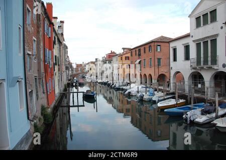 Bunte Hausfassaden und Wolken am Himmel reflektieren Das Wasser des Kanals und einige Boote vertäuten Die Lagune von Chioggia in der Nähe von Venedig Stockfoto