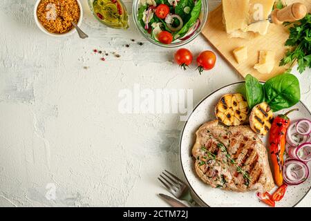 Hausgemachtes gegrilltes Schweinesteak mit Gemüse, Gewürzen und Parmesankäse auf betontem Hintergrund. Draufsicht, Kopierbereich. Stockfoto