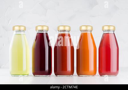 Gemüse- und Fruchtsäfte großes Set in Glasflaschen mit Kappe in Reihe auf weißem Holztisch im hellen Innenraum, Vorlage für Verpackung, Werbung Stockfoto