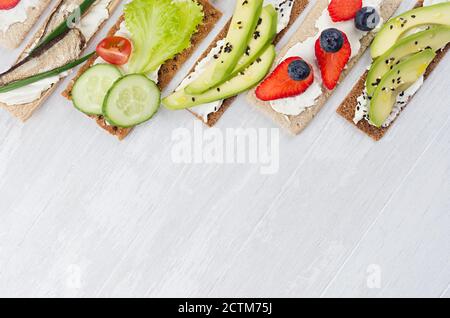 Auswahl an frischen Sommerfrüchten gesunde Vorspeisen von Chips Brot mit frischem Gemüse, reifen Früchten, Fischkonserven, Frischkäse auf weißem Holz bo Stockfoto