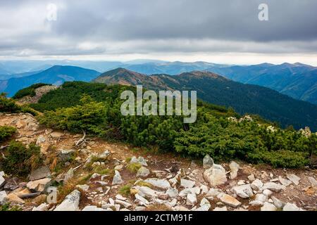 Blick von der Spitze eines Berges. wolkige Herbstlandschaft. Bergkette hinter dem Tal in der Ferne. Dramatisches Wetter in farbenfroher Landschaft Stockfoto