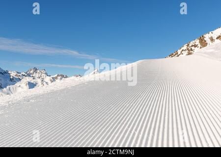 Nahaufnahme gerade Reihen von frisch präparierten Skipisten mit hell strahlender Sonne und klarem blauen Himmel Hintergrund. Schneebedeckter Berg Stockfoto