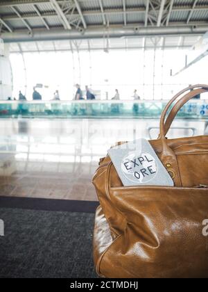 Tasche und Reisepass mit Motivationszitat "Entdecken" in einem flughafenterminal mit Reisenden im Hintergrund Stockfoto