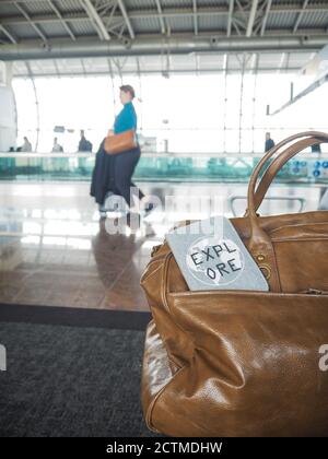 Tasche und Reisepass mit Motivationszitat "Entdecken" in einem flughafenterminal mit Reisenden im Hintergrund Stockfoto