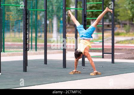 Junger männlicher Athlet, der einen Handstand mit Griffen an einem macht Outdoor-Fitnessraum oder Sportanlage in einem Gesundheits-und Fitness Konzept Stockfoto