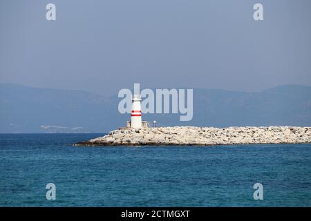 Leuchtturm Turm auf einem Steinsteg in azurblauem Meer gegen Neblige Berge Stockfoto