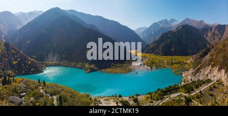 Herbstpanorama des Issyk Bergsees. Herbststimmung. Der türkisfarbene See ist von Bergen mit vergilbten Bäumen umgeben. Stockfoto