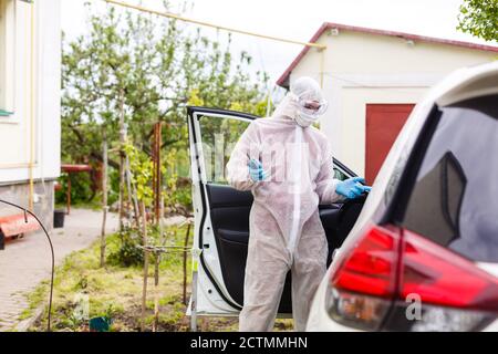 Mann mit Schutzkleidung, Handschuhen, OP-Maske und Gesichtsschutz, der Covid-19 Coronavirus an einem anderen Mann im Auto testet. Stockfoto