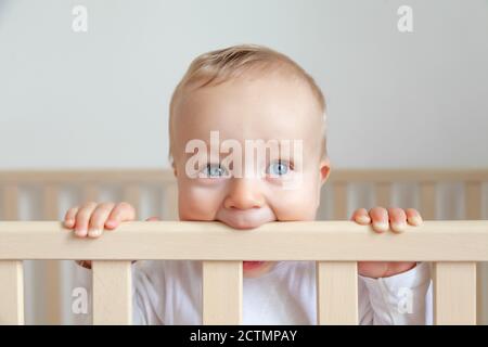 Blonde niedliche kleine Baby beißen Holzbett Kopfteil Stockfoto