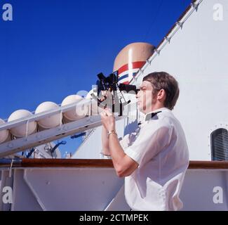 1960er Jahre, historisch, draußen auf dem Deck eines Kreuzschiffes, ein Schiffs-Navigator mit einem Sextant, ein marines Instrument zur Messung des Winkels zwischen zwei Objekten, dem Horizont und einem Himmelskörper, wie der Sonne oder Mond. Sie wurden - und werden auch heute noch - in der Navigation genutzt, um "in Sicht zu nehmen; d.h. um Breiten- und Längengrad zu bestimmen und so die Position des Schiffes auf dem Ozean zu bestimmen. Stockfoto