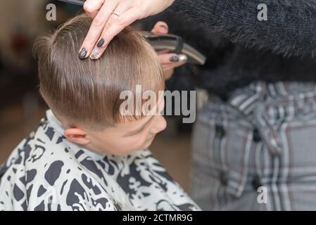 Happy Calm kaukasischen Schuljunge sitzt in einem Friseurladen und schneidet Haare. Stockfoto