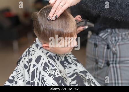 Happy Calm kaukasischen Schuljunge sitzt in einem Friseurladen und schneidet Haare. Stockfoto