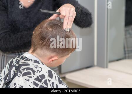 Happy Calm kaukasischen Schuljunge sitzt in einem Friseurladen und schneidet Haare. Stockfoto