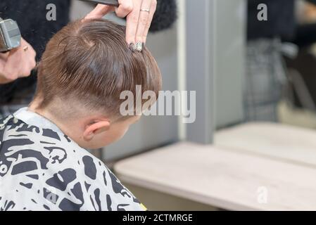 Happy Calm kaukasischen Schuljunge sitzt in einem Friseurladen und schneidet Haare. Stockfoto