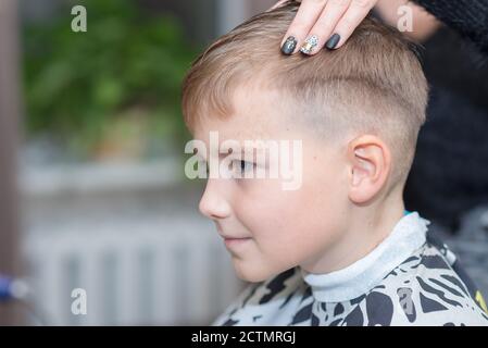 Seitenansicht Happy Calm kaukasischen Schuljunge sitzt in einem Friseurladen und schneidet Haare. Stockfoto