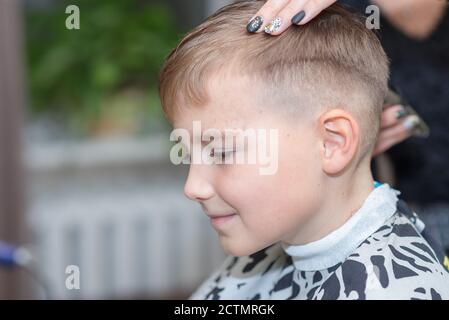 Seitenansicht Happy Calm kaukasischen Schuljunge sitzt in einem Friseurladen und schneidet Haare. Stockfoto