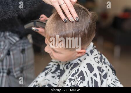 Happy Calm kaukasischen Schuljunge sitzt in einem Friseurladen und schneidet Haare. Stockfoto