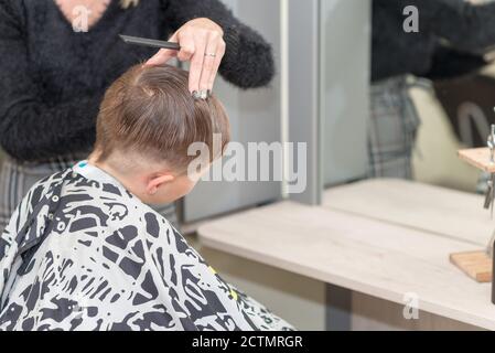 Happy Calm kaukasischen Schuljunge sitzt in einem Friseurladen und schneidet Haare. Stockfoto