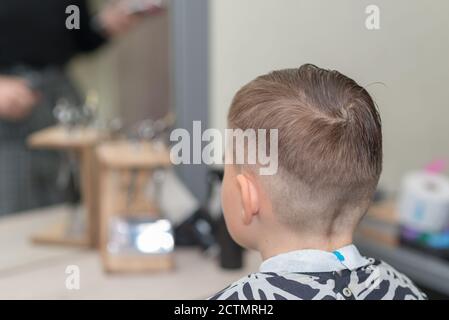 Happy Calm kaukasischen Schuljunge sitzt in einem Friseurladen und schneidet Haare. Stockfoto