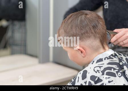 Happy Calm kaukasischen Schuljunge sitzt in einem Friseurladen und schneidet Haare. Stockfoto