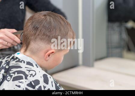 Happy Calm kaukasischen Schuljunge sitzt in einem Friseurladen und schneidet Haare. Stockfoto