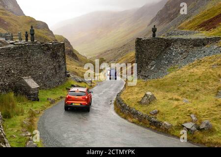 Honister Pass Summit - malerische Bergpassstraße im Lake District, England - Autos vorbei an Skulpturen auf beiden Seiten der Straße bei Honister Slate Mine Stockfoto