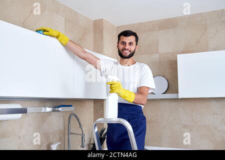 Mann, der die Küchenoberfläche hoch oben putzt und auf einer Leiter steht. Reinigungsdienstkonzept Stockfoto