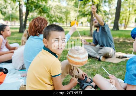 Portrait von lächelnden Schuljunge sitzt unter Klassenkameraden im Park und Halten Planetenmodell bei Astronomie Lektion Stockfoto