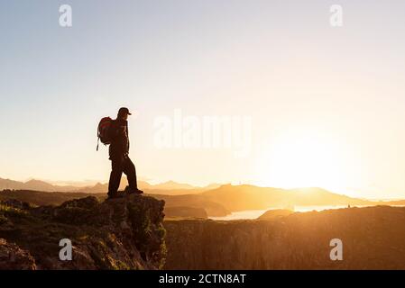 Seitenansicht eines anonymen Wanderers mit Rucksack auf dem er steht Rock in den Bergen und genießen Sie erstaunliche Sonnenuntergang während des Urlaubs Stockfoto