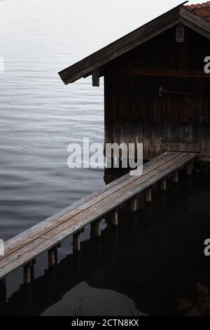 Blick auf verwitterte hölzerne Bootsschuppen und Planken pier über plätschernden dunklen See Wasser bei bewölktem Wetter in Herbsttag Stockfoto