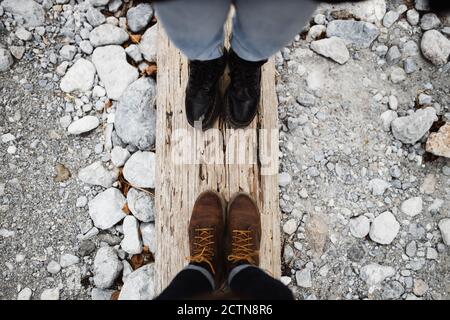 Von oben der Ernte anonymen männlichen und weiblichen Reisenden in Stiefel stehen auf verwittertem Holzbalken auf steinigem Boden Stockfoto