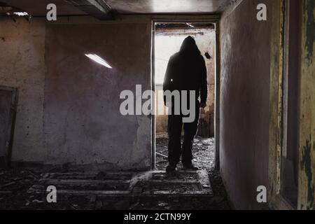 Ein Mann mit Kapuze, der in der Tür eines zerstörten, verlassenen Hauses steht Stockfoto