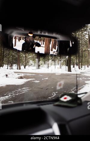 Anonymous Reisende Auto fahren auf schneebedeckten Asphalt Landschaft unter Nadelbäumen Holz im Wintertag in den USA Stockfoto