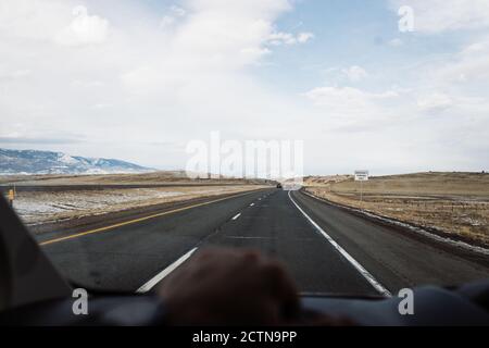 POV schoss durch die Windschutzscheibe des Autos, das von anonymen Reisenden gefahren wurde Auf Asphalt Autobahn durch Wüstental in Richtung Bergrücken Im Wintertag in den USA Stockfoto