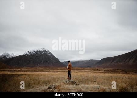 Rückansicht des nicht erkennbaren männlichen Forschers, der auf Felsen und steht Genießen Sie die Berglandschaft im Herbst in den schottischen Highlands Stockfoto