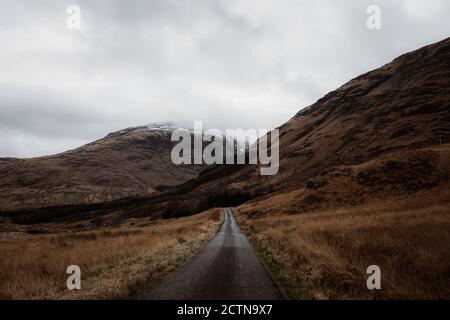 Straße zwischen Tal und herrlichem Blick auf felsigen Berg Top mit Schnee im Herbst in den schottischen Highlands Stockfoto