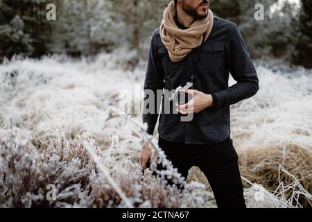 Zugeschnittenes unkenntlich Mann mit Fotokamera stehend in Wiese mit Gefrorenes Gras im Winter in den schottischen Highlands Stockfoto