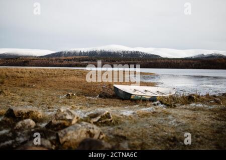 Einsames Boot, das am Ufer in der Nähe eines ruhigen Sees im Hintergrund festgemacht ist Der bergigen Landschaft in den schottischen Highlands Stockfoto